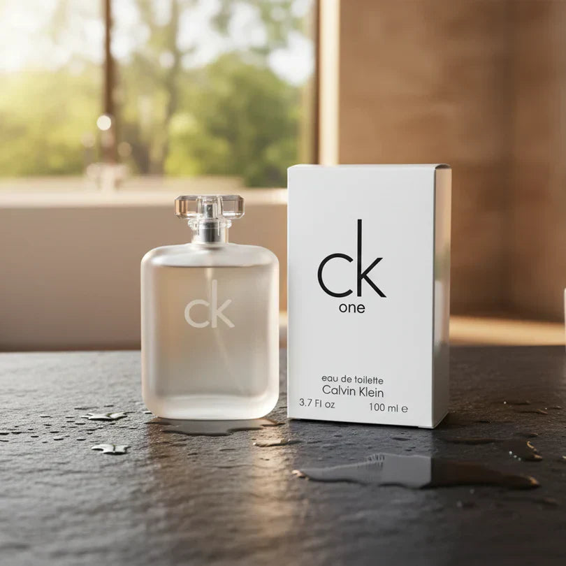 Calvin Klein CK One perfume bottle with original packaging displayed on a reflective surface, featuring a clean minimalist design and a blurred outdoor background, representing a fresh unisex fragrance.