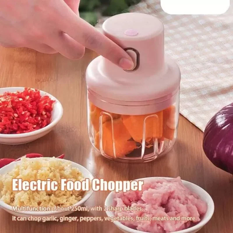 Compact electric food chopper with freshly chopped vegetables and ingredients arranged on a wooden table.