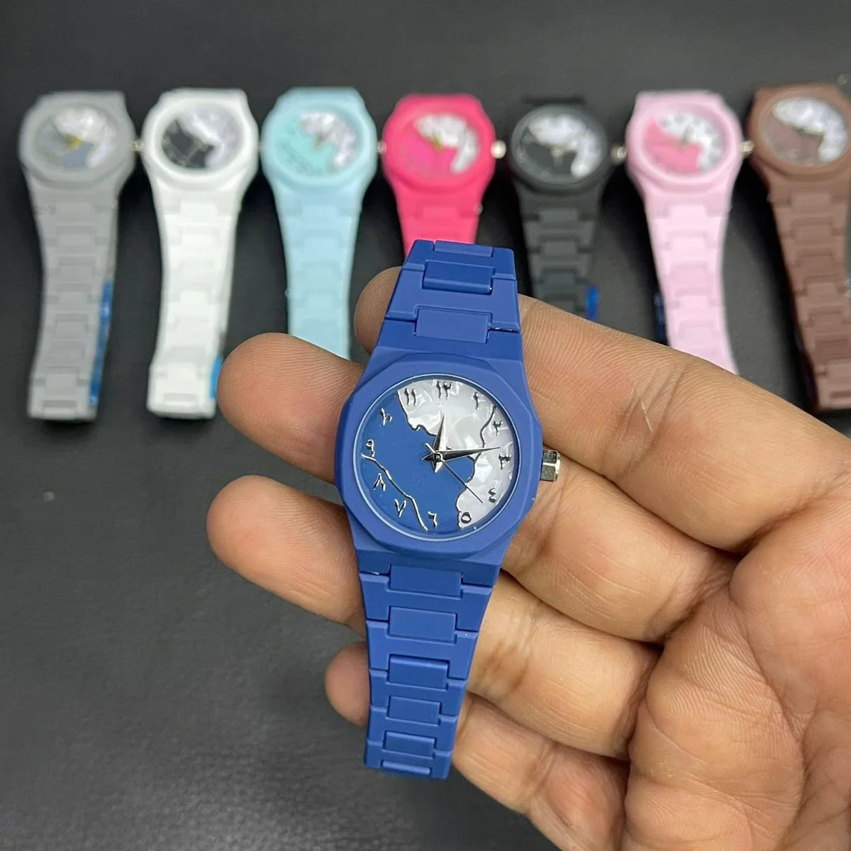 Close-up of a stylish blue analog wristwatch with a matching blue strap and unique artistic dial design. Displayed in hand with multiple color variations in the background, suitable for women, girls, and everyday fashion wear.