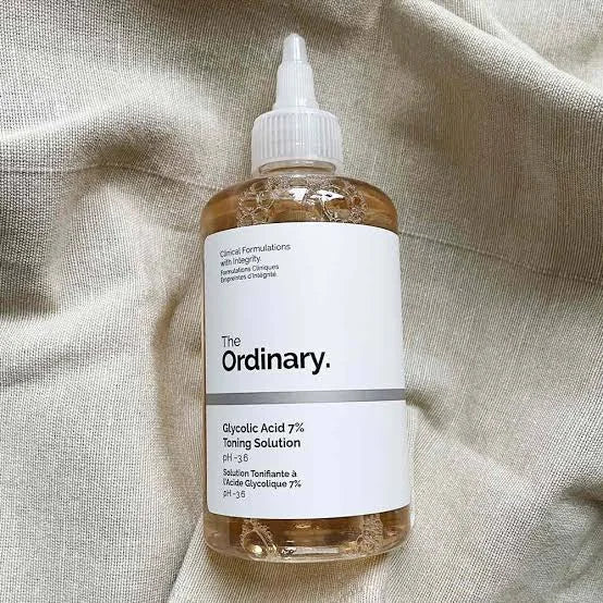 The Ordinary Glycolic Acid 7% Toning Solution bottle displayed on a textured beige background. Skincare exfoliating toner designed to improve skin texture, remove dead skin cells, enhance radiance, and support a smoother-looking complexion.