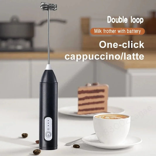 Black battery-powered electric milk frother on a kitchen counter beside a cup of coffee and cake, designed for creating rich foam for lattes, cappuccinos, hot chocolate, and other beverages.