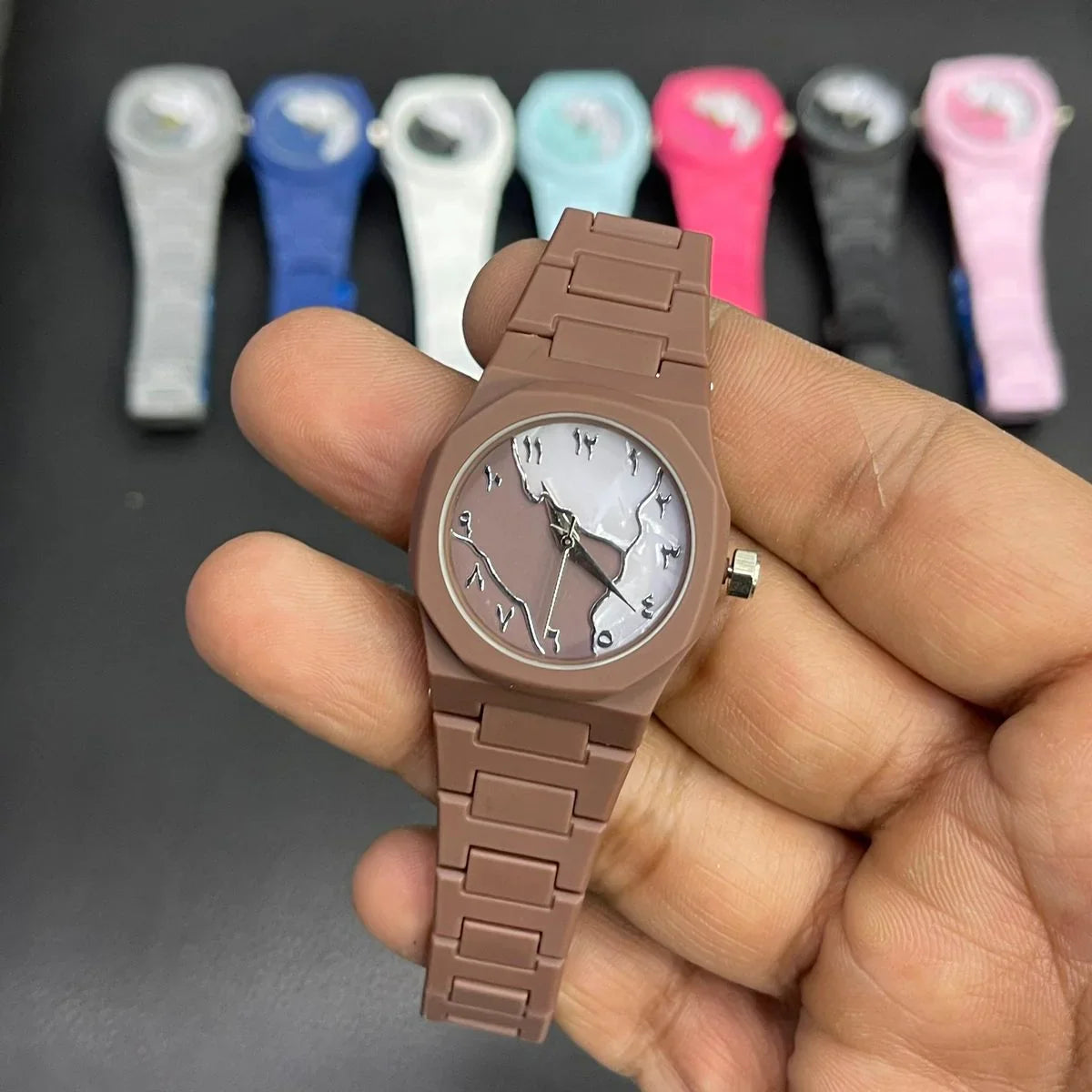 Close-up of a brown women's wrist watch featuring a marble pattern dial, silver hands, and a matching silicone strap, with multiple color variants displayed in the background.