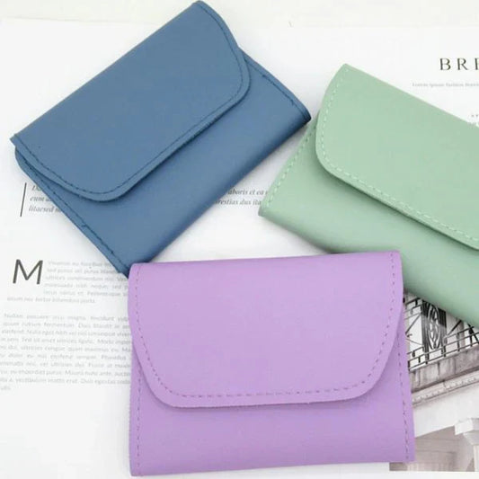 Three compact wallets in blue, green, and purple displayed on a magazine background, featuring a slim design for storing cash, cards, and everyday essentials.