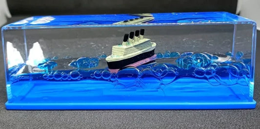 Decorative cruise ship model displayed inside a transparent case with a blue water effect, featuring detailed craftsmanship and a stylish design suitable for home or office décor.