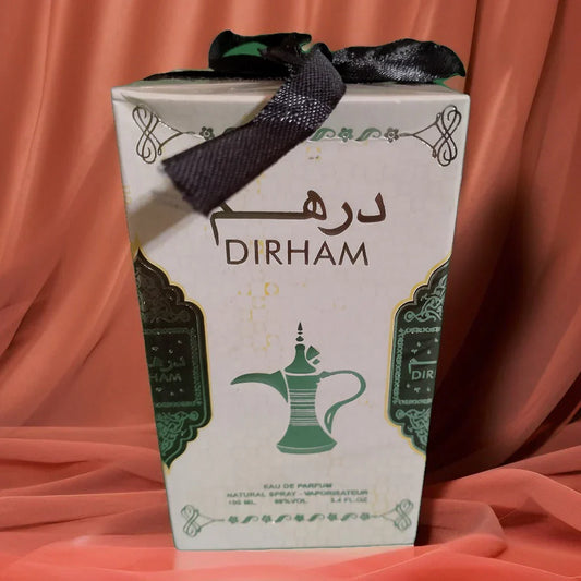 Dirham perfume gift box wrapped with a green ribbon and displayed on a soft pink fabric background, highlighting elegant packaging and a premium fragrance presentation suitable for gifting.