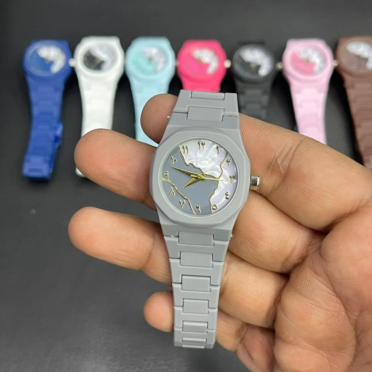 Close-up of a gray women's wrist watch featuring a marble pattern dial, gold hands, and a matching silicone strap, with multiple color options displayed in the background.