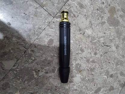 Heavy-duty metal spray nozzle attachment for a cordless pressure washer placed on a tiled floor. Durable black and brass design with adjustable spray settings for car washing, driveway cleaning, patio maintenance, and garden watering applications.