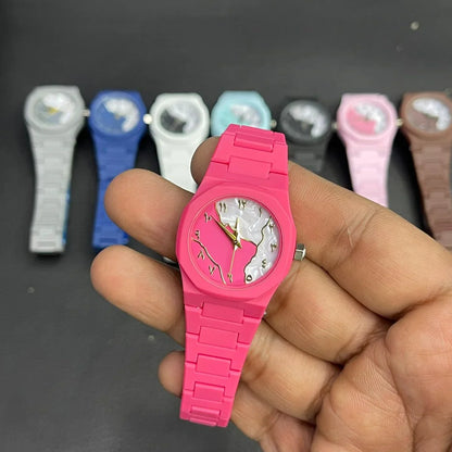 Close-up of a pink women's wrist watch featuring a marble pattern dial, gold hands, and a matching silicone strap, with multiple color variants displayed in the background.