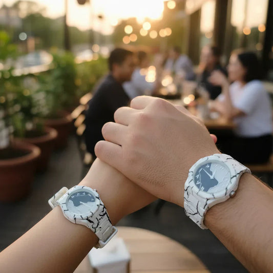 Couple wearing matching white marble pattern wrist watches with white straps while holding hands at an outdoor café during sunset, showcasing a stylish his and hers watch set.