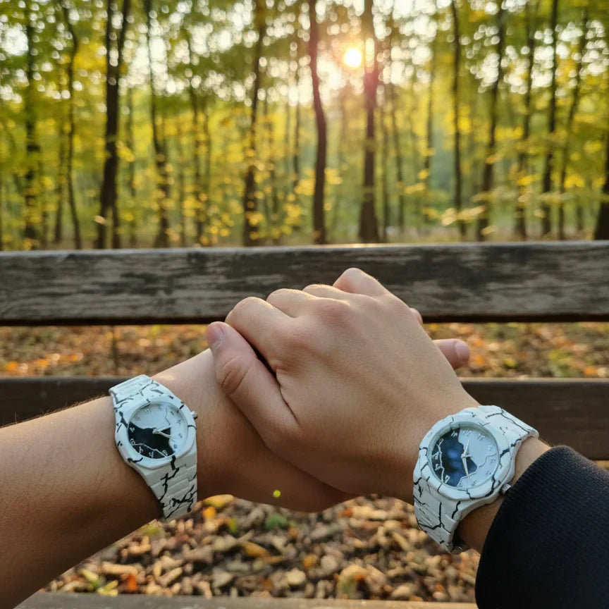 Couple wearing matching white marble pattern wrist watches while holding hands on a park bench at sunset, showcasing a stylish his and hers watch set with elegant round dials.