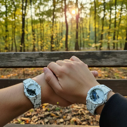 Couple wearing matching white marble pattern wrist watches while holding hands on a park bench at sunset, showcasing a stylish his and hers watch set with elegant round dials.